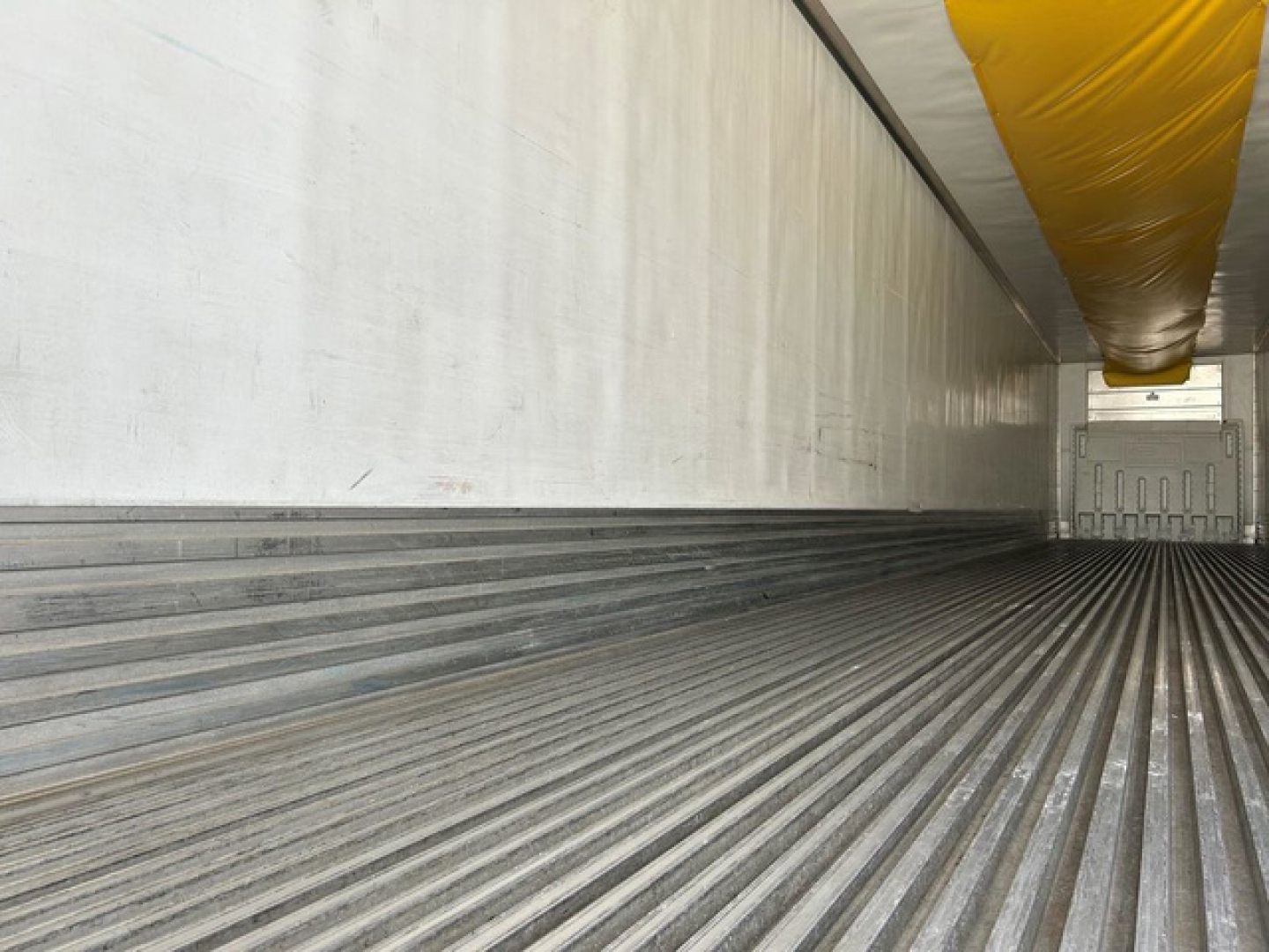 Trailer interior showing ribbed floor and side walls of a refrigerated trailer with yellow ceiling lining.