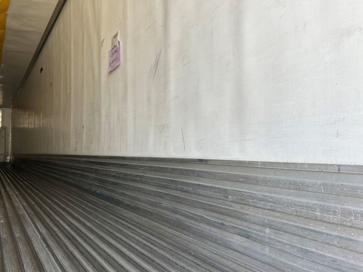 Trailer interior showing ribbed metal flooring and vertical side wall with a pink note posted.