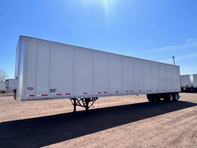 Trailer side view showing 53' dry van trailer with white walls and tandem axles under clear sky.