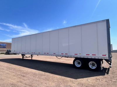 Trailer side view showing a white Wabash trailer with dual rear axles and reflective tape along the lower edge.
