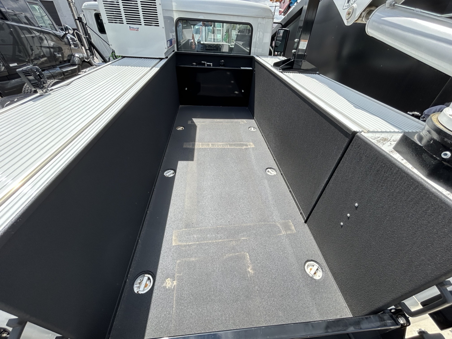 Mack MD6 bed area showing flatbed with tie-down points and textured bed surface; rear cab in background with tailgate notch.