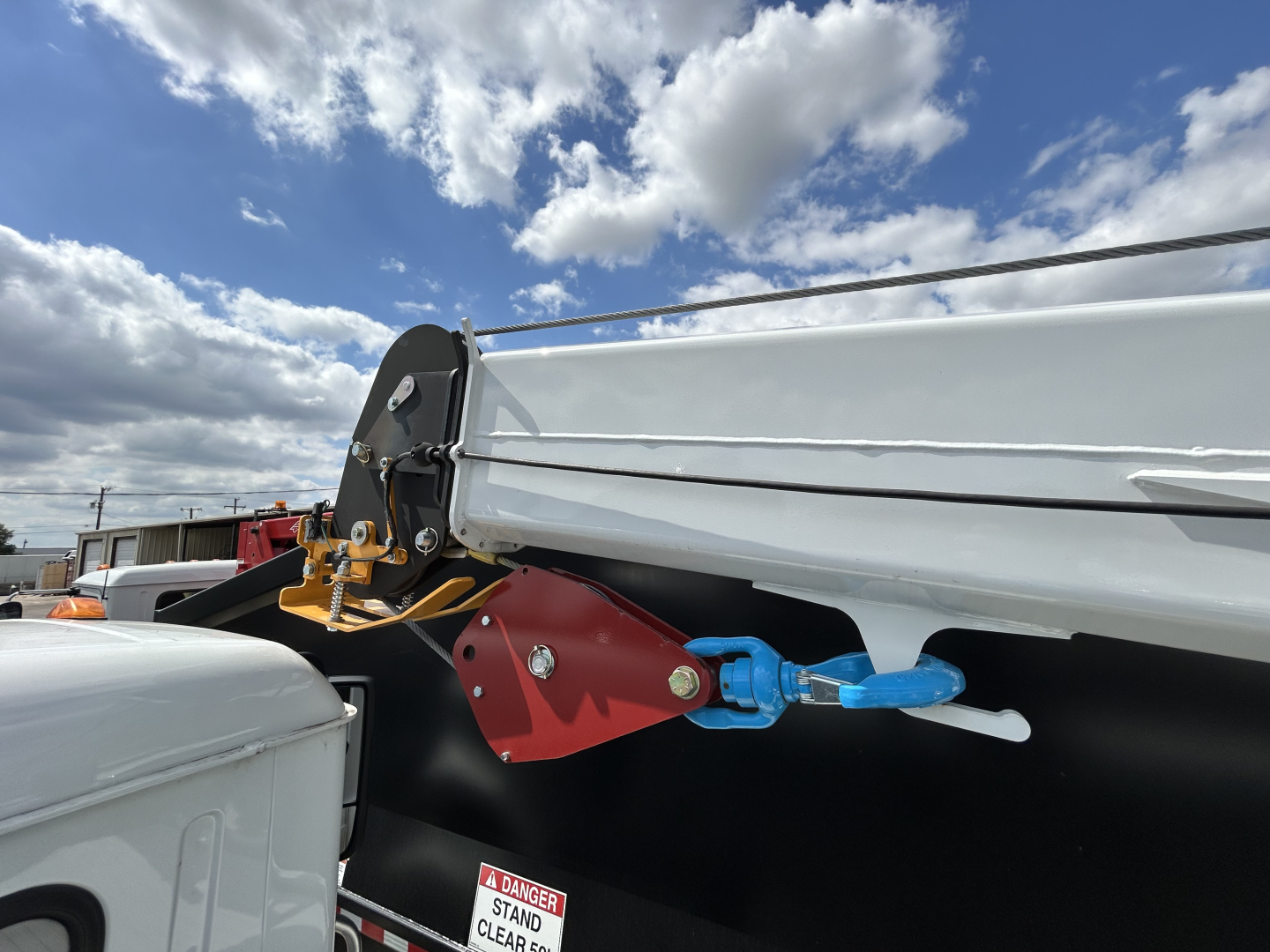 Rear view of a new Mack MD6 trucks showing a blue hitch pin and red hitch mount attached to a side rail. Part of a white dump body and black chassis visible.