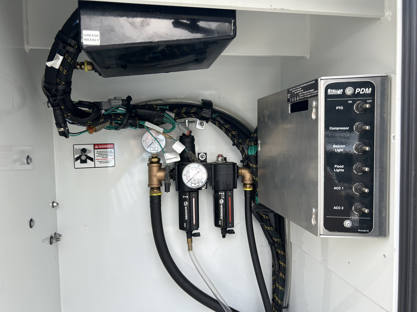 Mack MD6 service body interior showing PDM control panel and hydraulic lines with gauges and valves.