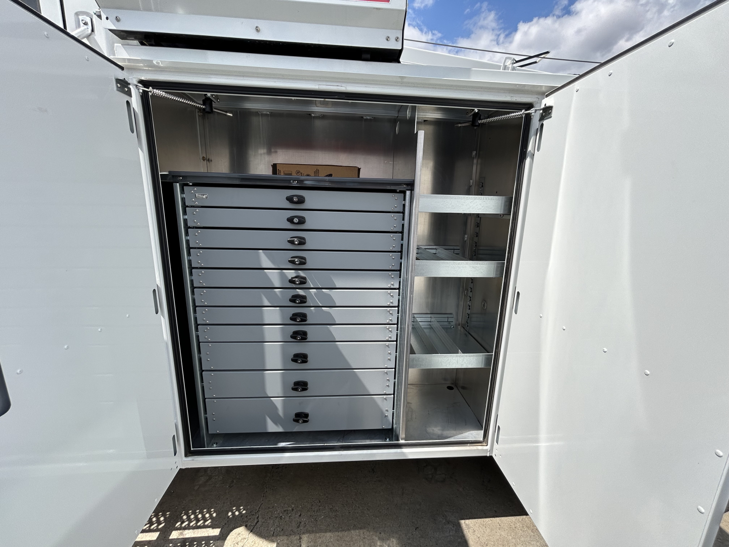 Storage cabinet inside service truck with multiple tool drawers and open shelving, mounted in a metal compartment.