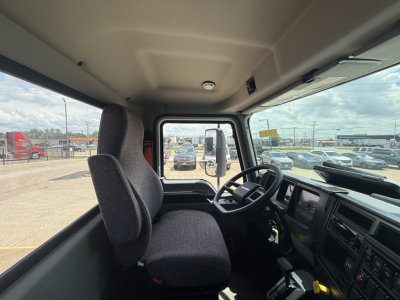 Mack MD6 cab interior showing steering wheel, dash, and two front seats; view through windshield with exterior lot in background.
