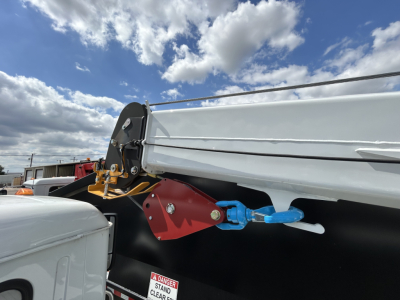 Rear view of a new Mack MD6 trucks showing a blue hitch pin and red hitch mount attached to a side rail. Part of a white dump body and black chassis visible.