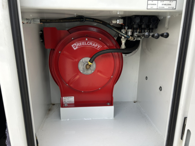 Red Reelcraft hose reel inside service truck storage bay with white interior. Visible labels include Reelcraft and small white placards with numbers.