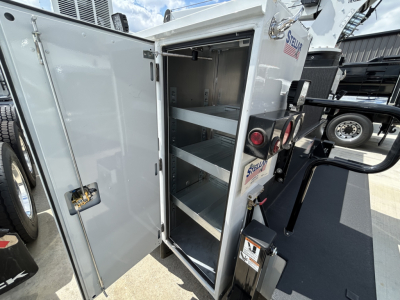 Service body vanes open showing shelving in compartment of 2025 Mack MD6 truck, with Spare/utility storage cabinet doors and hydraulic lift components visible.