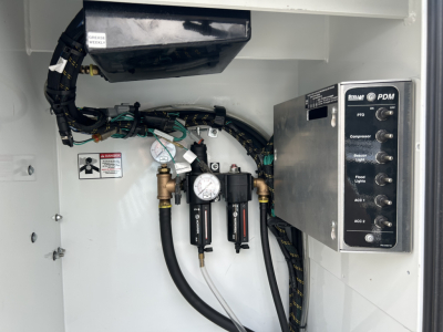Mack MD6 service body interior showing PDM control panel and hydraulic lines with gauges and valves.