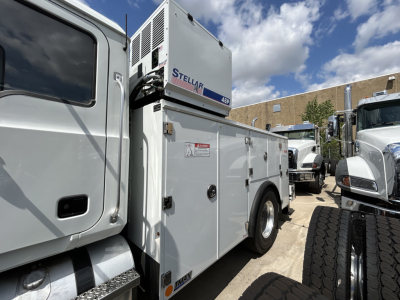 Mack MD6 service truck utility body with Stellar Gen set unit mounted on top, visible doors and compartments, side tires, and part of other trucks in background.