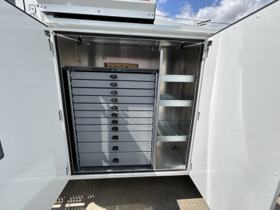 Storage cabinet inside service truck with multiple tool drawers and open shelving, mounted in a metal compartment.