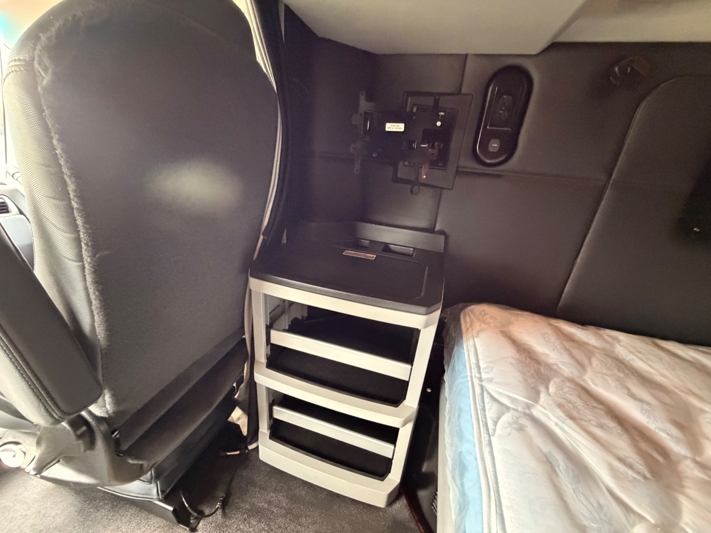 Kenworth T680 truck cab interior showing a small rolling cabinet with shelves and a mattress visible on right side.