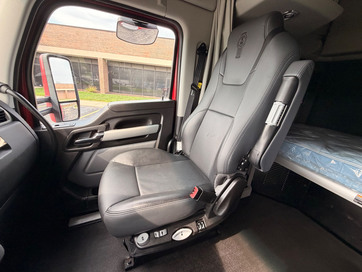 Kenworth T680 cabin interior showing driver's seat with controls and sleeper bunk in background.