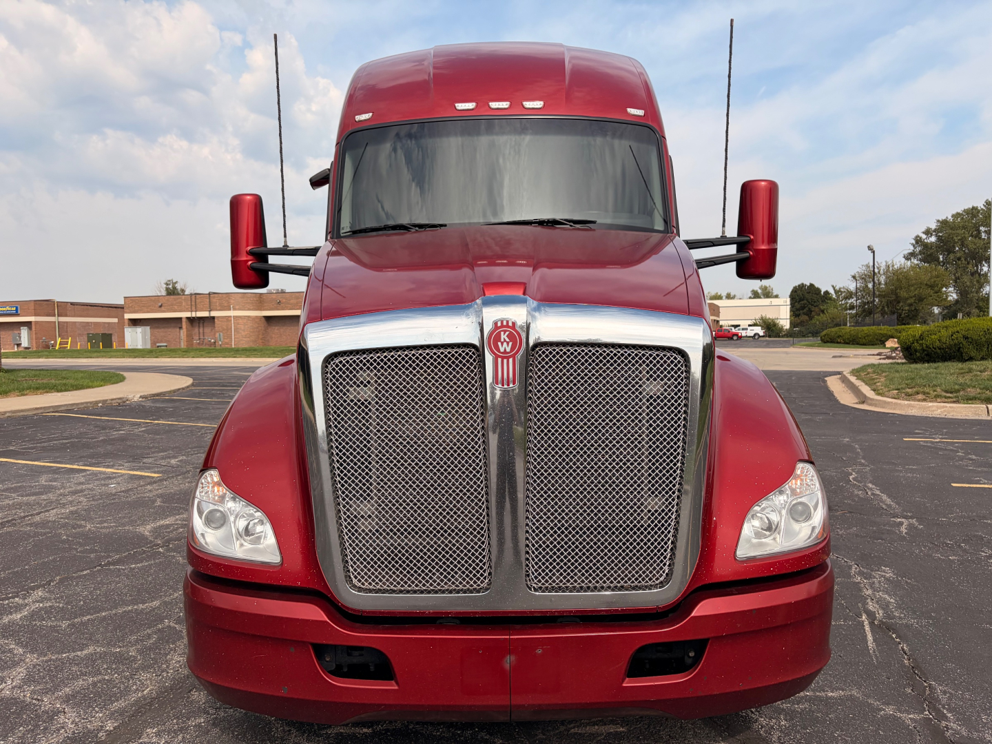 Kenworth T680 front view showing large black mesh grille, chrome surround, red body, and dual mirrors.