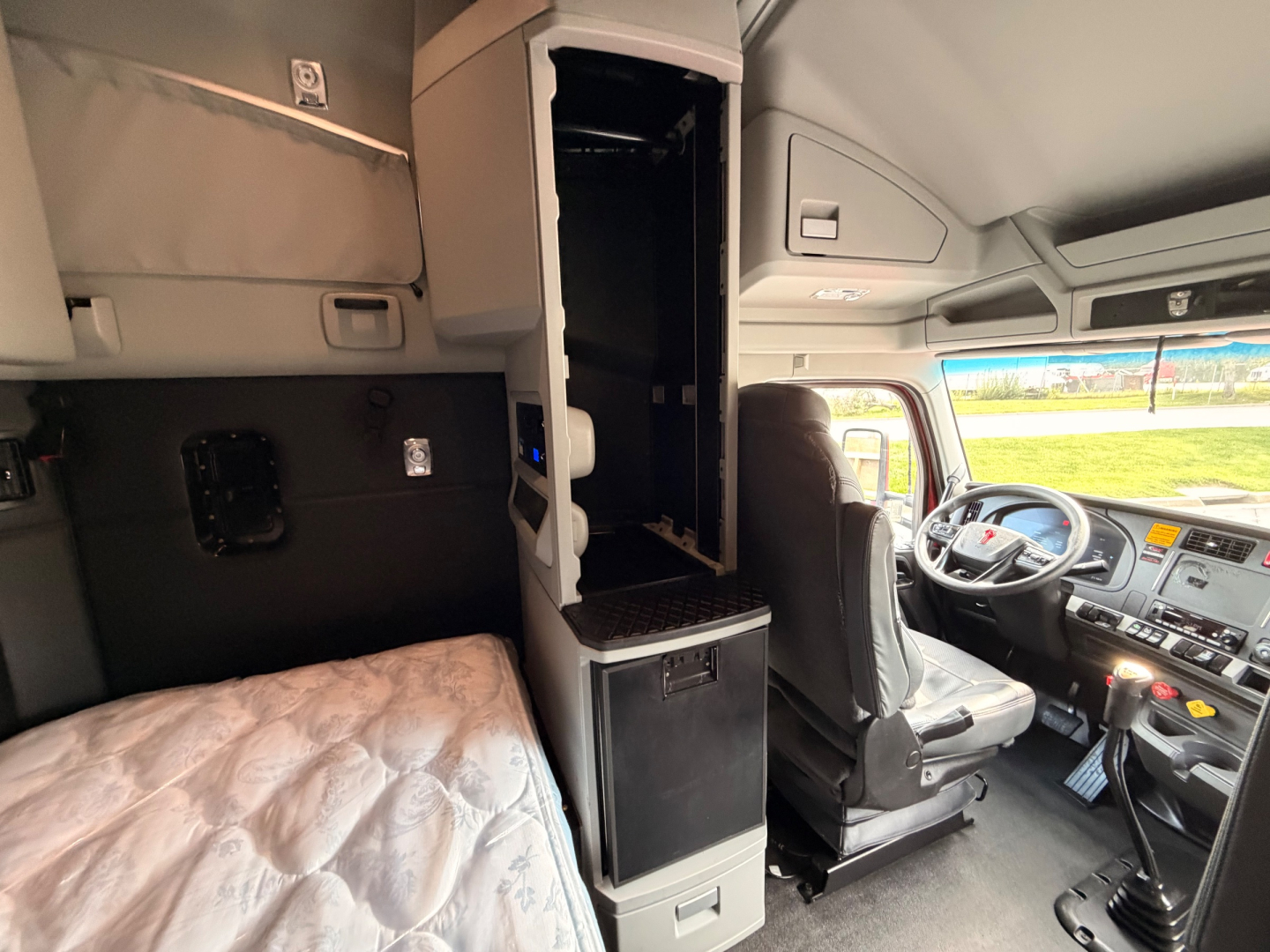 Cab interior of a Kenworth T680 truck showing driver seat, center console, storage compartments, and sleeping area visible.