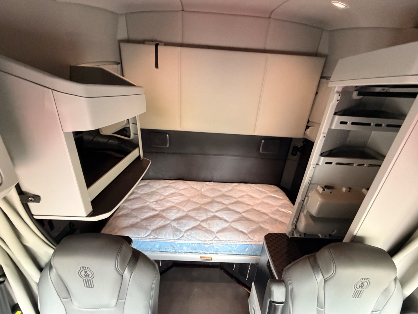 Kenworth T680 sleeper cab interior showing bunk area with mattress, overhead storage, and refrigerator in cabin.