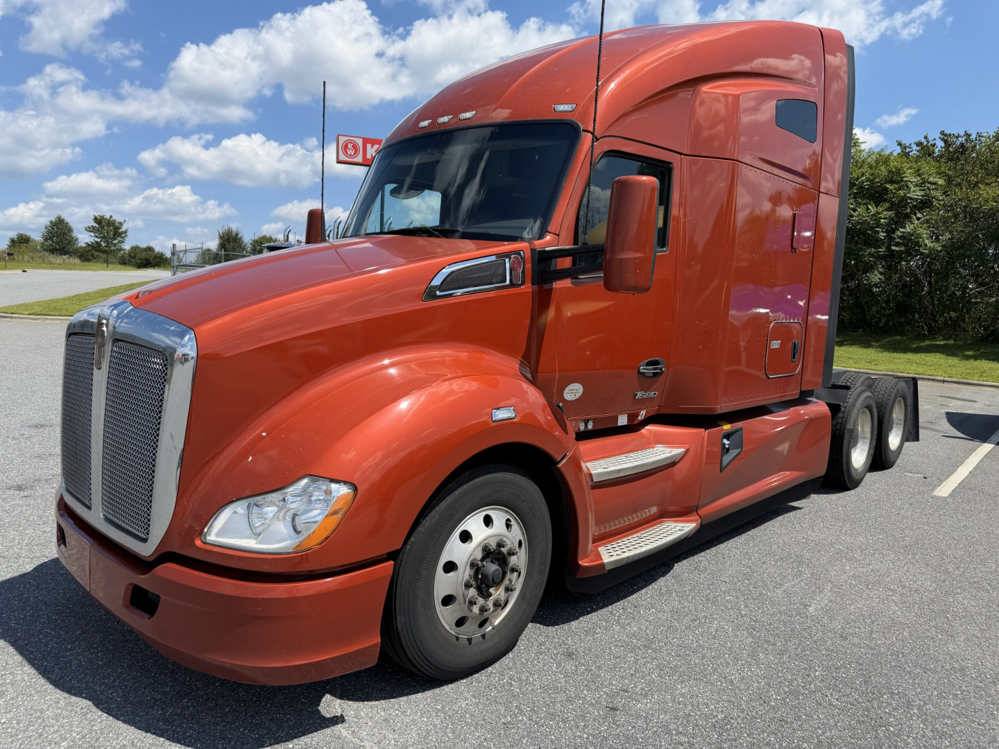 Kenworth T680 sleeper tractor in orange, side view showing front grille, cab, and dual rear axles.