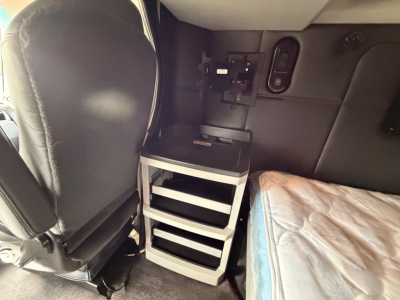 Kenworth T680 truck cab interior showing a small rolling cabinet with shelves and a mattress visible on right side.