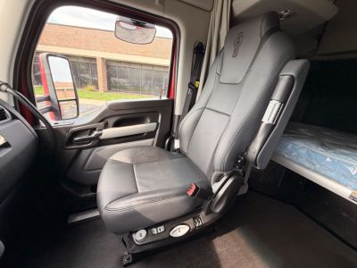 Kenworth T680 cabin interior showing driver's seat with controls and sleeper bunk in background.