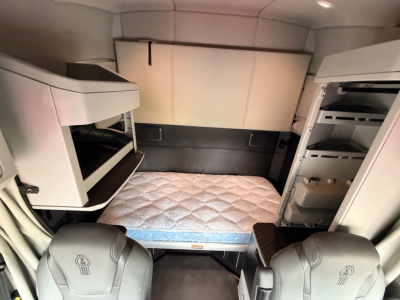 Kenworth T680 sleeper cab interior showing bunk area with mattress, overhead storage, and refrigerator in cabin.