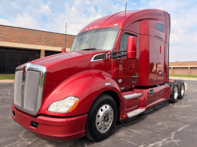 Red 2022 Kenworth T680 conventional sleeper truck in a parking lot, side view showing front grille, cab, and dual rear axles.