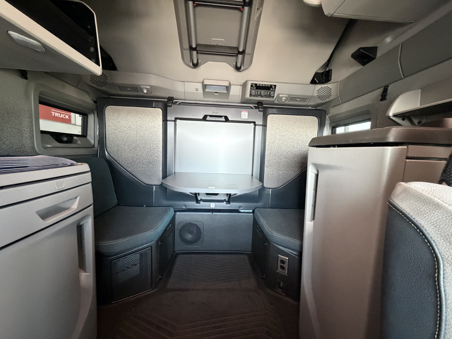 Volvo VNL cab interior showing sleeper area with seats, overhead storage, and controls above windshield.