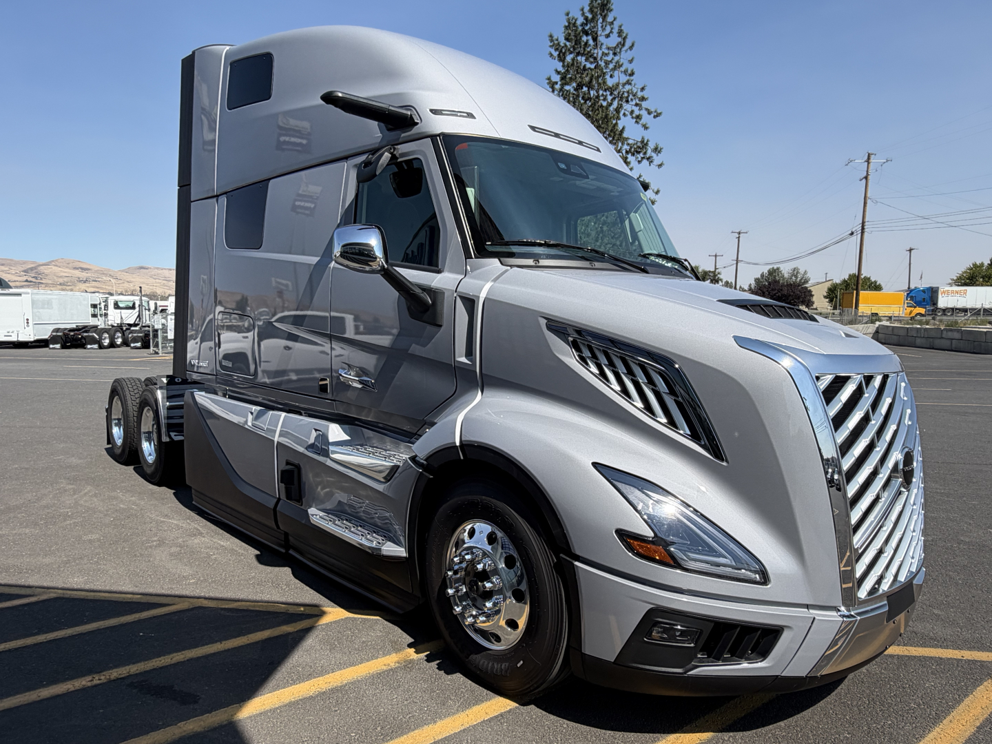 Volvo VNL64T860 sleeper cab truck in silver with chrome mirrors and grille, front view, parking lot background.
