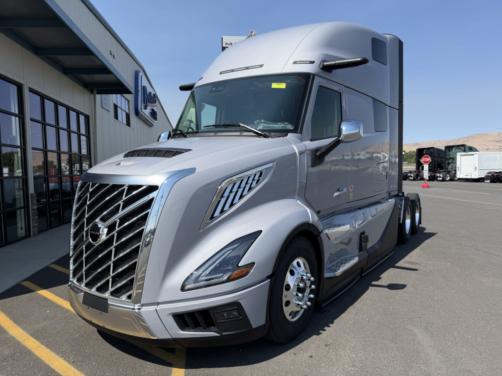 Volvo VNL64T860 sleeper cab truck in silver, front-left view with grille, large headlights, and chrome wheels.