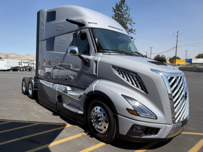 Volvo VNL64T860 sleeper cab truck in silver with chrome mirrors and grille, front view, parking lot background.