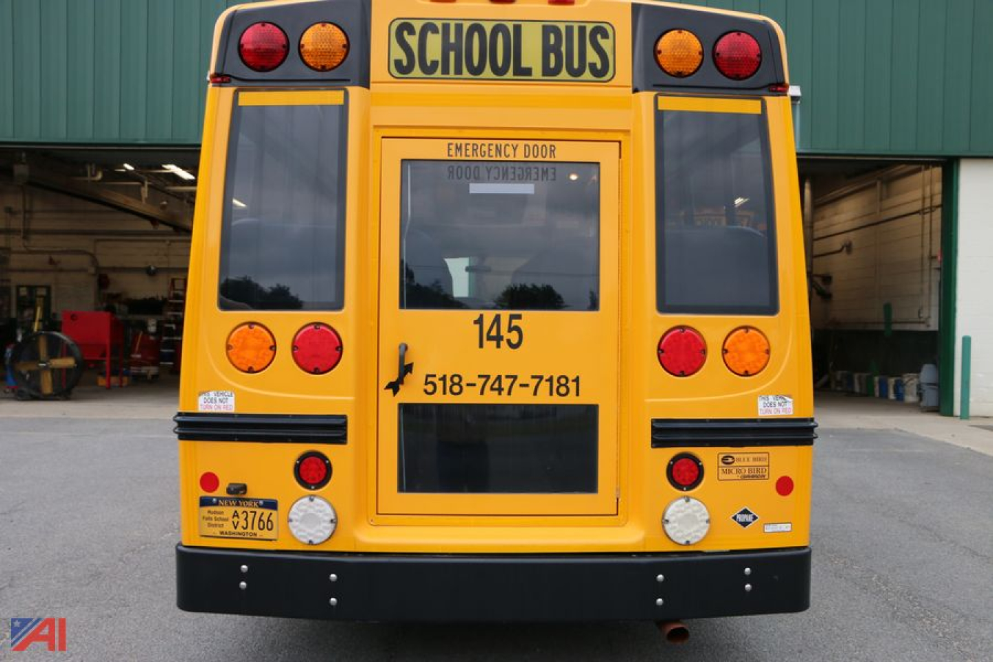 Rear view of a yellow 2015 Ford E450 school bus with 'SCHOOL BUS' sign, emergency lights, bus number 145, and phone number 518-747-7181 on the back panels.