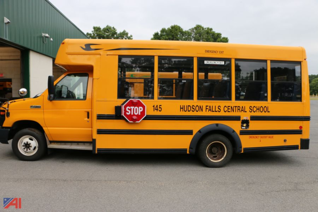 Blue text and numbers on yellow school bus: STOP sign extended, Hudson Falls Central School, 145, emergency exit label, windowed side with several passenger windows.