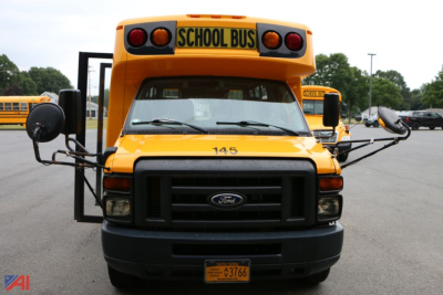 School bus front view showing Ford emblem, yellow body, black grille, 'SCHOOL BUS' sign, and orange license plate holder.