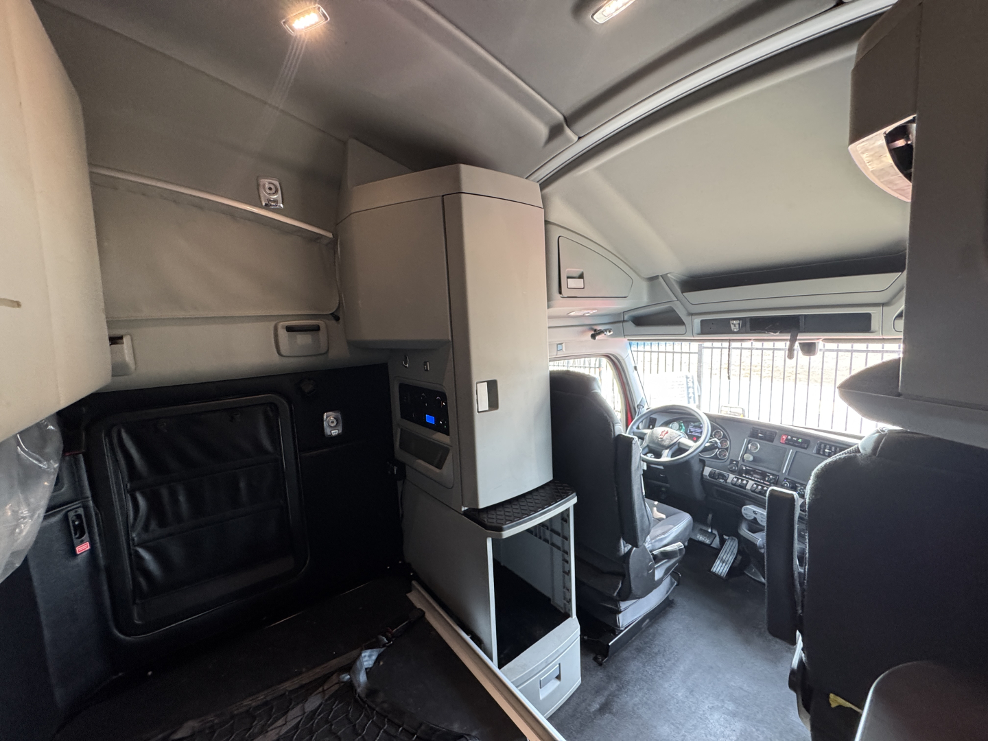 Kenworth T680 cab interior showing driver seat, dashboard, and overhead cabinet with control panel.