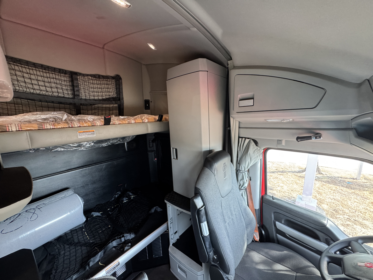 Cabin interior of a Kenworth truck showing bunk area and storage cabinet with seating in the foreground.