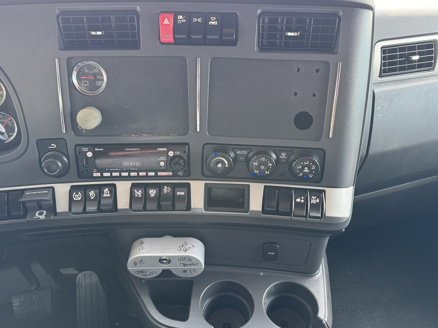 Dashboard of a Kenworth truck cab with gauges, air vents, controls, and a center console; visible text includes hazard button, climate controls, and empty instrument panels.