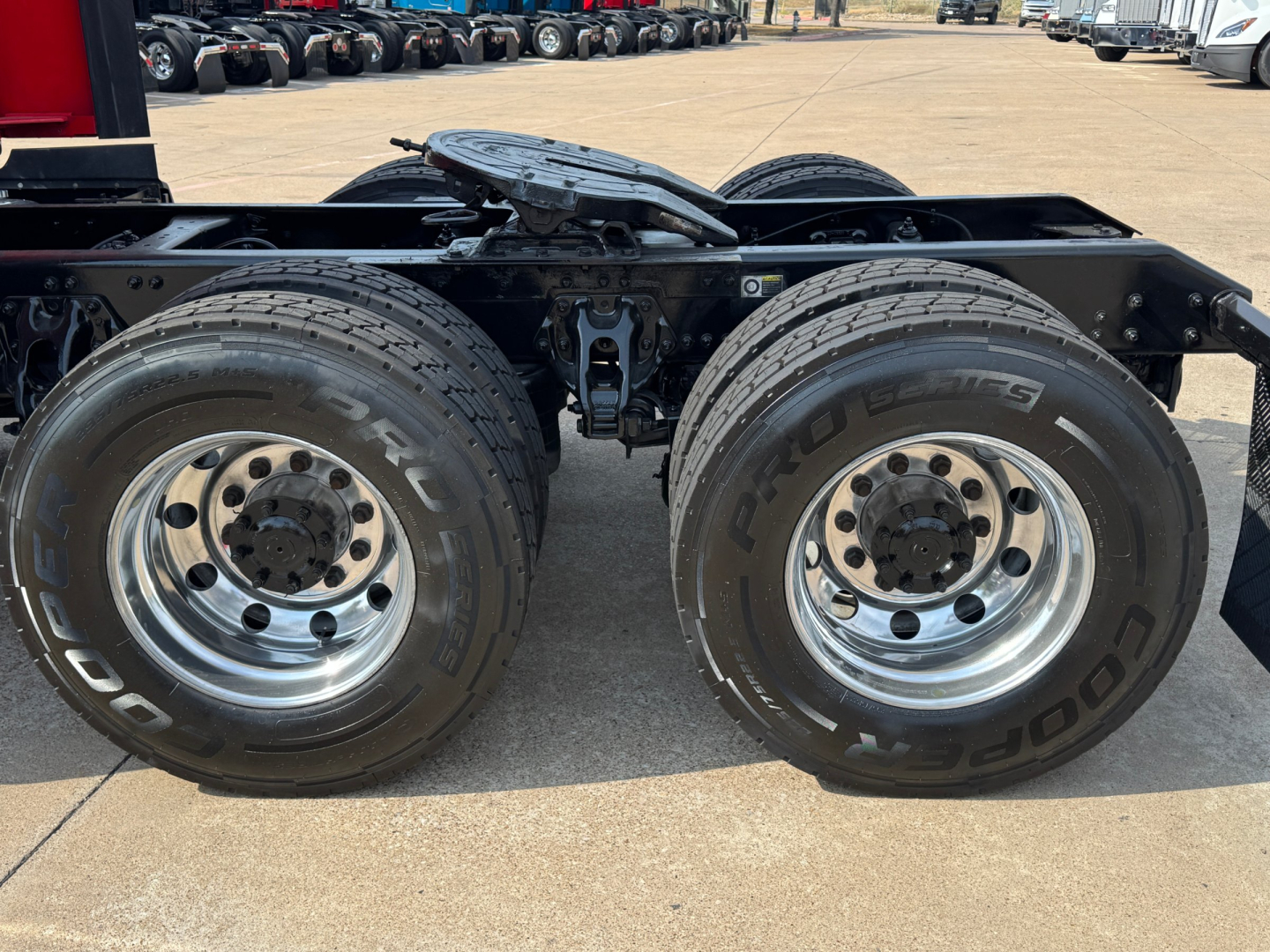 Kenworth T680 rear axle and dual tires on a concrete lot, chrome wheels, black frame, visible tires with Cooper Prodigy branding, no cab in view.