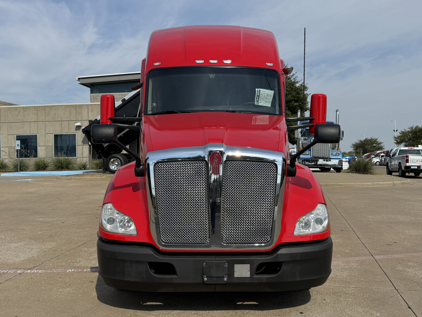 Kenworth T680 front view showing large chrome grille, red cab, black bumper, and side mirrors.