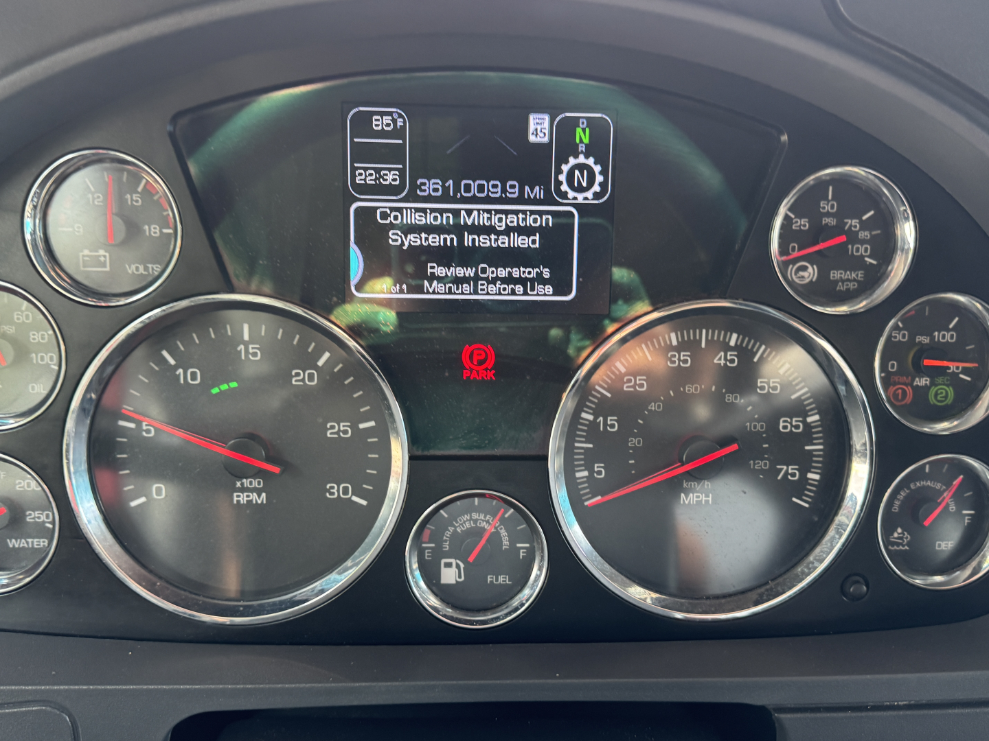 Kenworth T680 instrument cluster showing dashboard gauges and center display with 'Collision Mitigation System Installed' text.