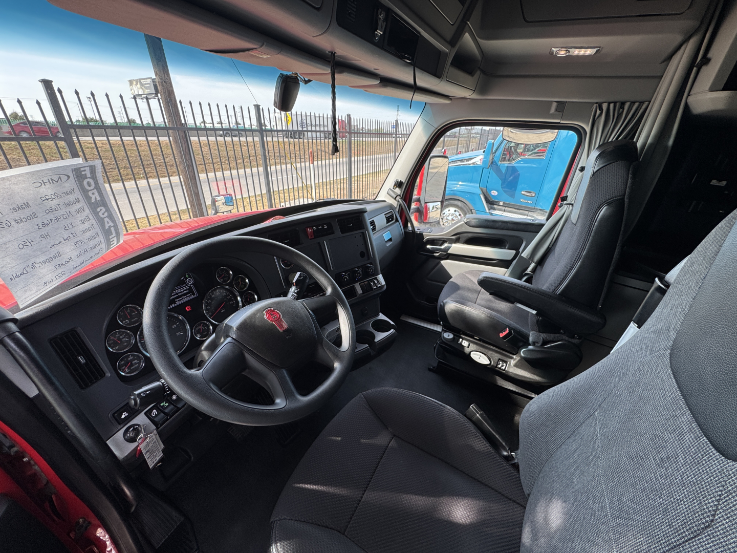 Kenworth T680 interior steering wheel and dashboard view from driver seat showing gauges, steering wheel with Kenworth badge, center console, and passenger seat.
