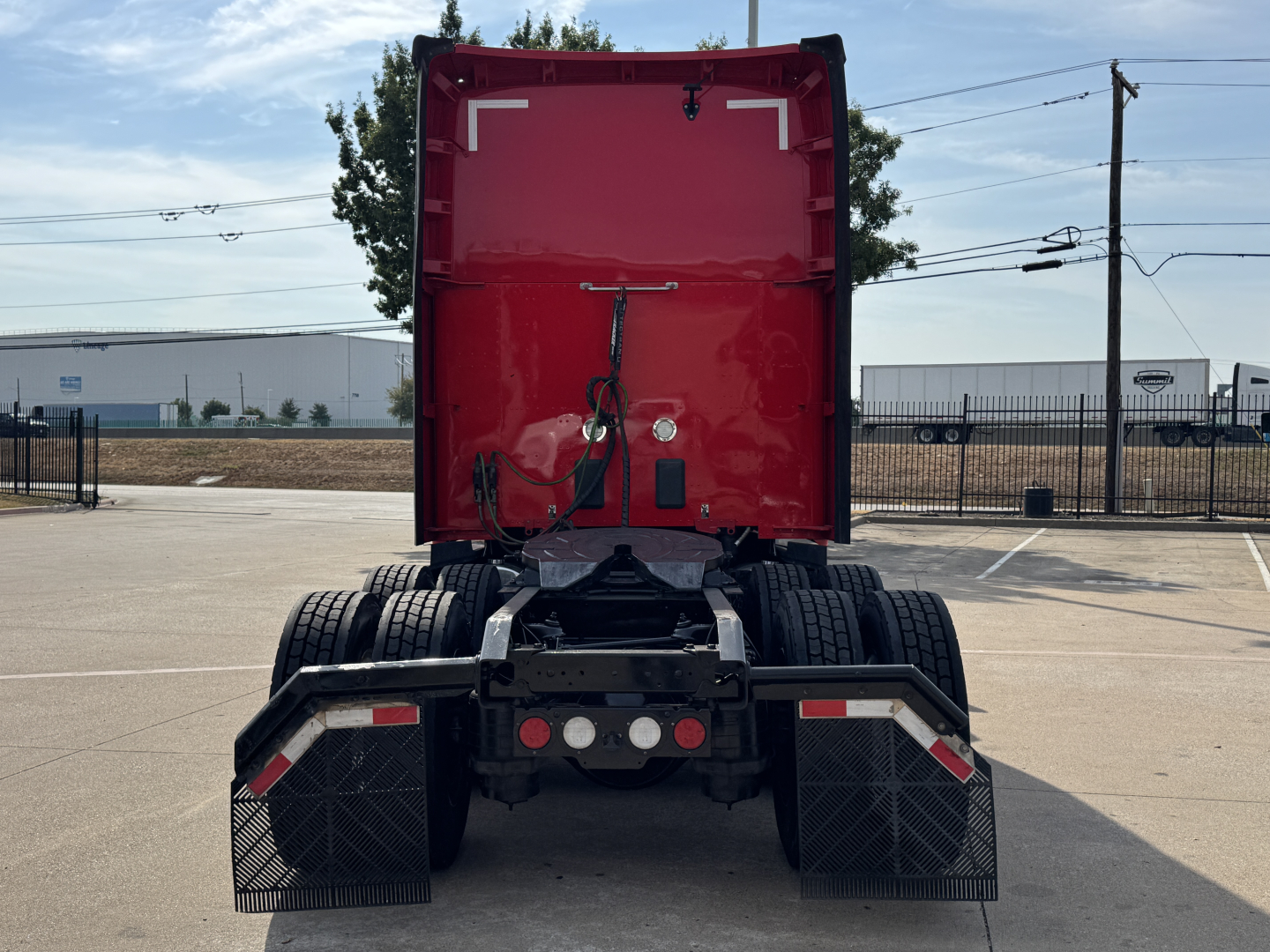Rear view of a red Kenworth T680 semi truck tractor showing dual rear wheels, mud flaps, and hitch with electrical connections.