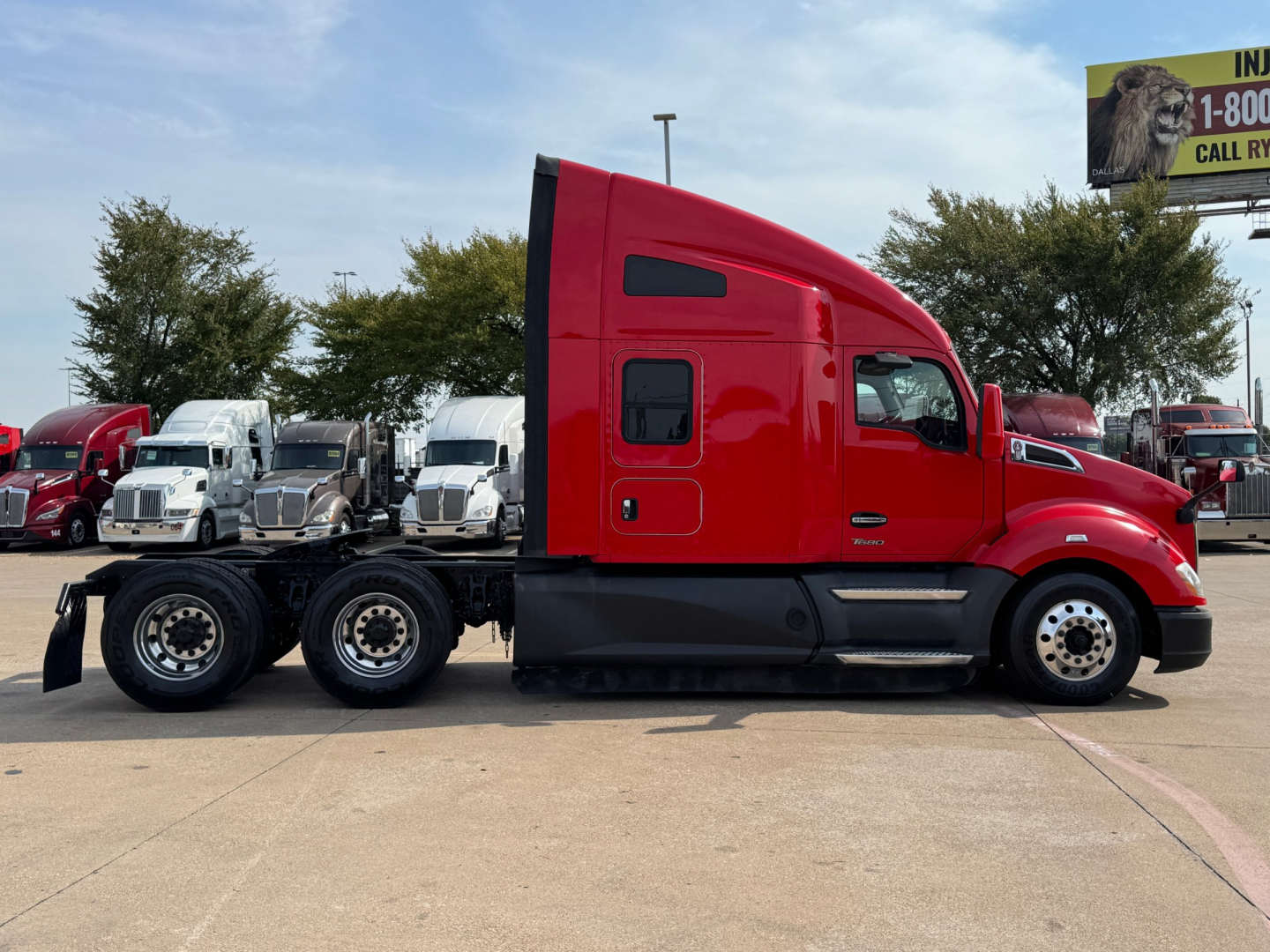 Kenworth T680 tractor in red side view showing chassis and cab profile, front wheels, and sleeper cab, with other trucks in background.
