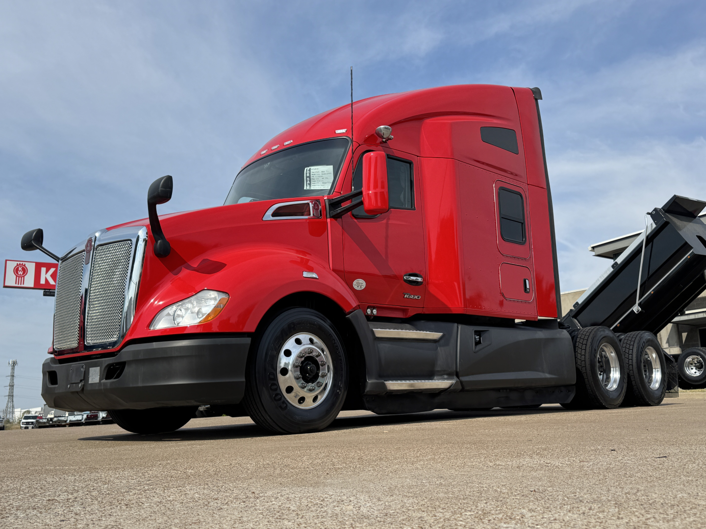 Kenworth T680 truck in red cab, side view, with a dump trailer bed attached; shows front grille, headlights, wheels, and side mirrors.