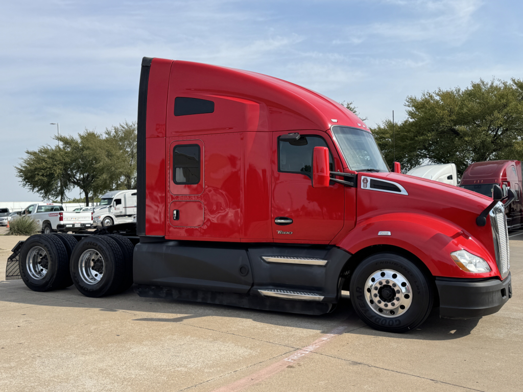 Red 2022 Kenworth T680 semi truck side view showing sleeper cab with black side skirt and dual rear axles.