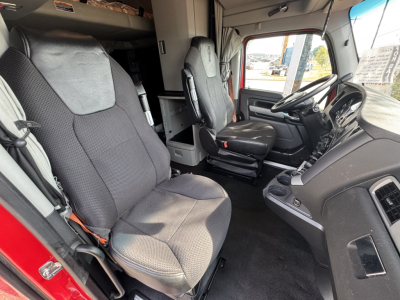 Kenworth T680 cab interior showing driver seat and passenger seat, steering wheel, dash with controls, and steps leading to sleeper area in view.