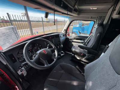 Kenworth T680 interior steering wheel and dashboard view from driver seat showing gauges, steering wheel with Kenworth badge, center console, and passenger seat.