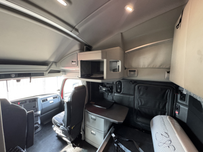 Cab interior of a 2022 Kenworth T680 sleeper with overhead storage, compact desk, drawers, and control panel visible.