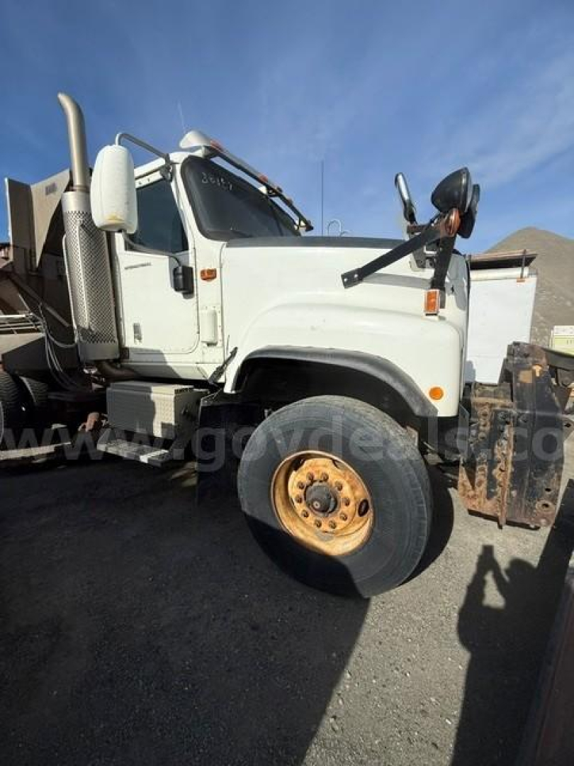 Front left side of a white International 5500i truck with plow, showing wheel, side mirror, and cab; no visible text clearly legible on components.