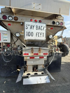 Back of a 2007 International 5500i plow truck showing rear lights, hitch, and a 'STAY BACK! 100 FEET' sign on the tailgate with dirt and utility wiring.