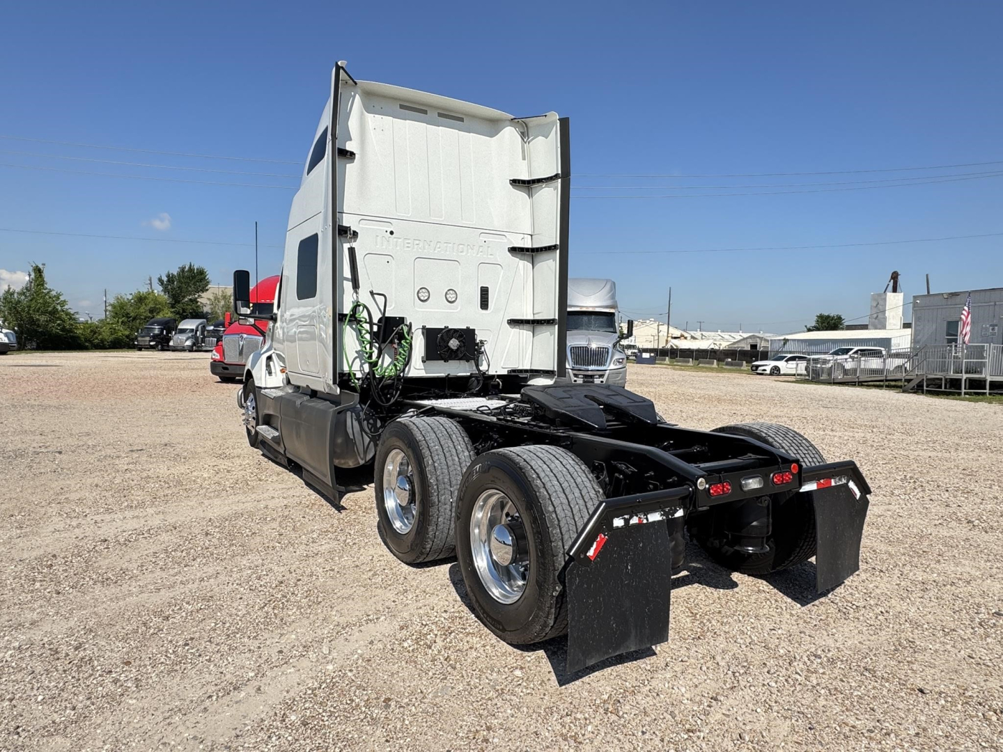Truck chassis back view showing dual rear axles and black mud flaps on a gravel lot.