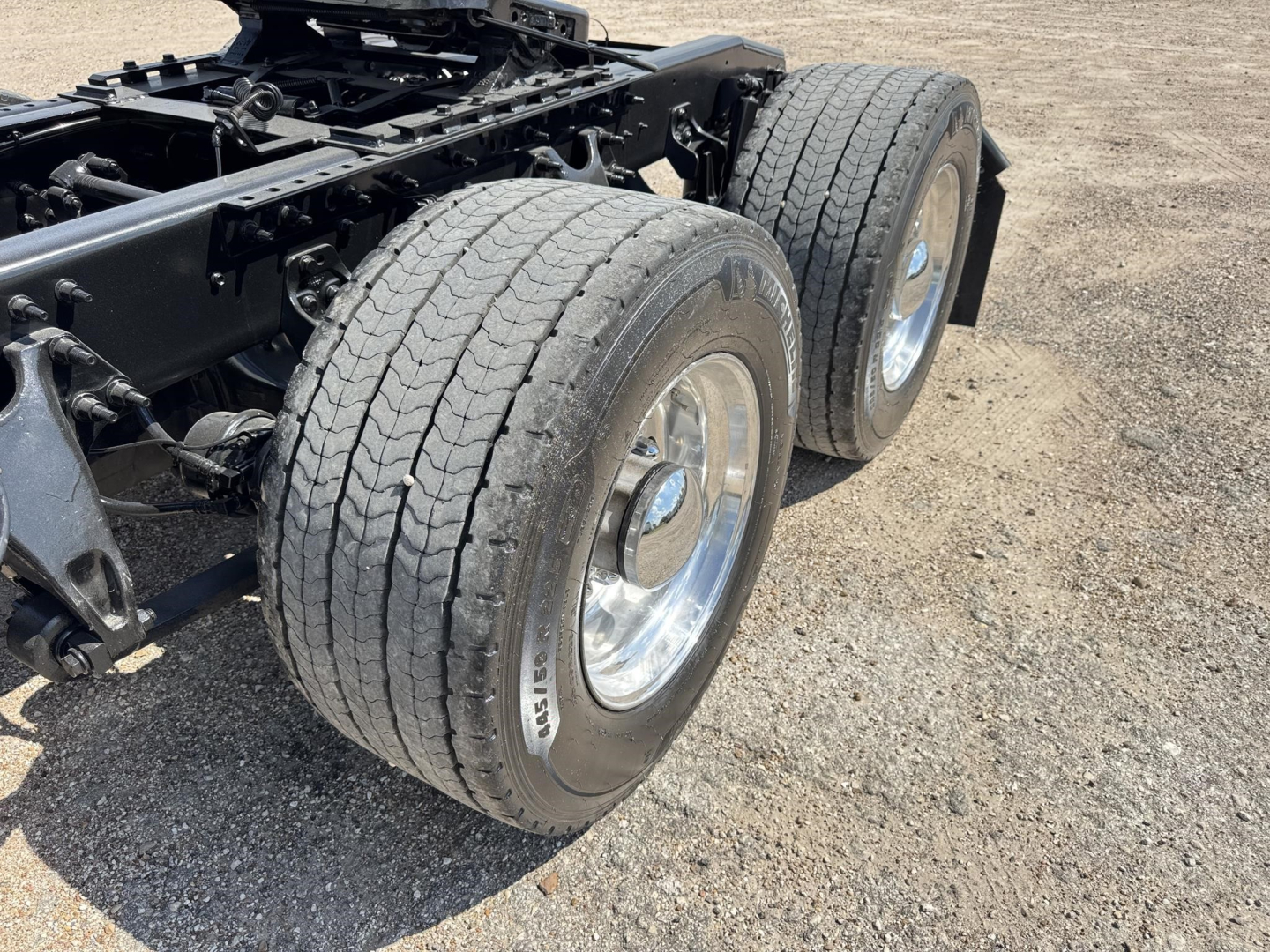Dual rear truck axles with large tires and chrome wheels on a heavy-duty chassis, showing wheel rims and suspension components.